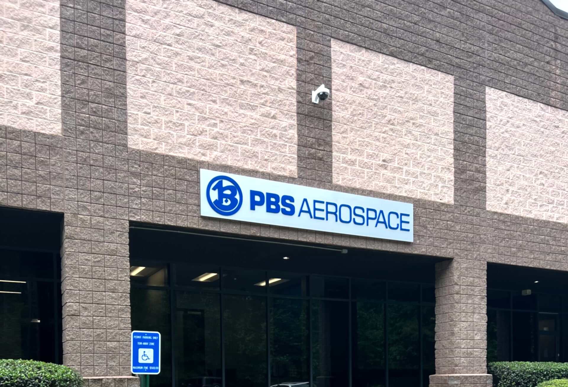 Exterior sign for PBS Aerospace in Roswell, GA featuring a brushed aluminum panel with painted, laser-cut acrylic lettering mounted to the face.