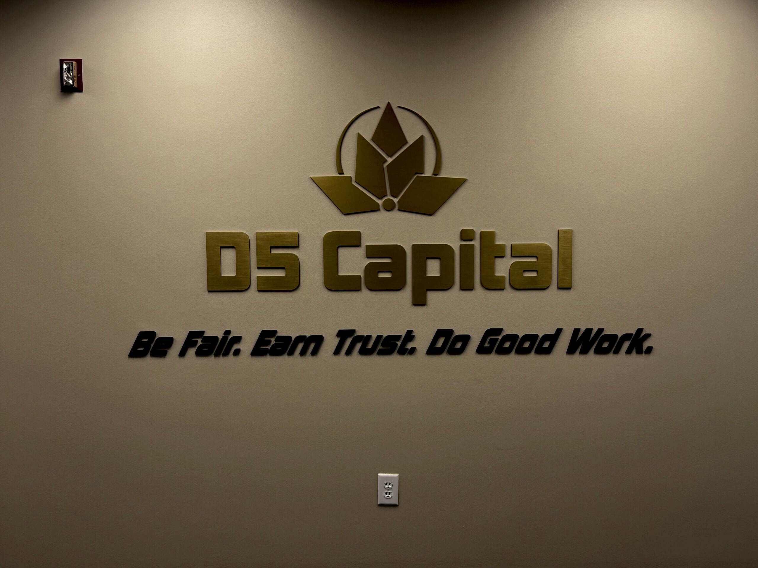 Custom 3D lobby sign for D5 Capital in Alpharetta, GA, featuring gold dimensional lettering, a matching logo, and the company tagline mounted on an interior wall.